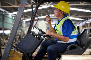 senior worker using walkie talkie and driving forklift truck in the factory