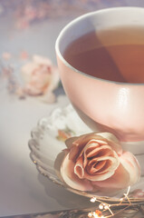 Pink mug with tea close-up. Part of a cup on a blurred background with rose flowers. Soft focus, vertical image