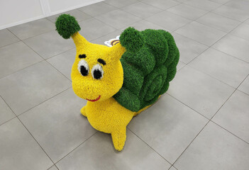 A funny artificial snail figurine topiary stands on the floor in a children's store