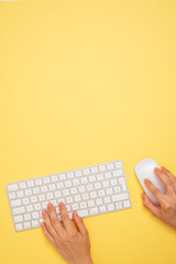 a person is using a computer keyboard with a mouse on a yellow background. Copy space