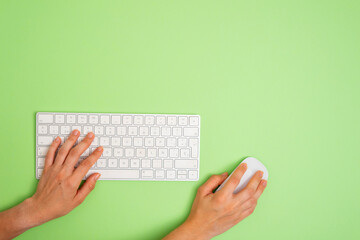 a person is using a computer keyboard with a mouse on a green background. Copy space