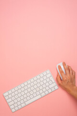 a person is using a computer keyboard with a mouse on a pink background. Copy space