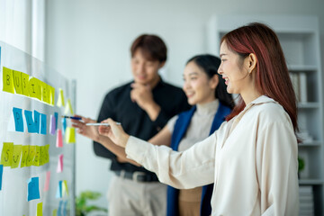 A woman is drawing on a whiteboard with her friends. The board has a lot of colorful sticky notes...