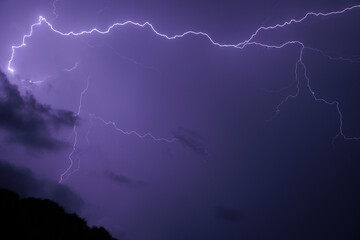 inquadratura dettagliata di vari fulmini che colorano il cielo di viola durante un intenso temporale notturno, in estate