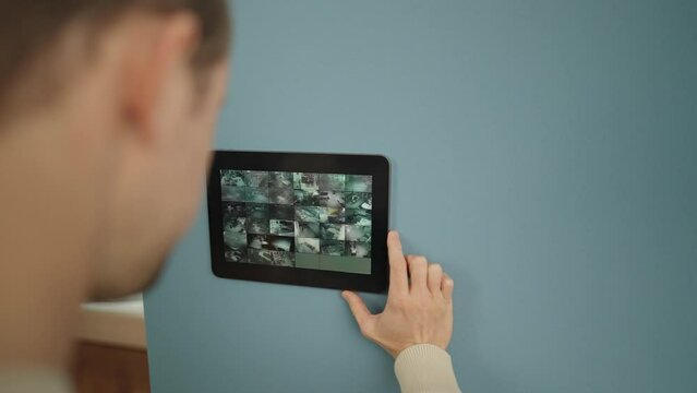 Over the shoulder shot - Unrecognisable man looking at security camera footage on smart home tablet mounted on the wall