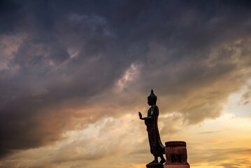 Stand big Buddha Statue in silhouette sun set Light background in park of Thailand temple.Yellow...