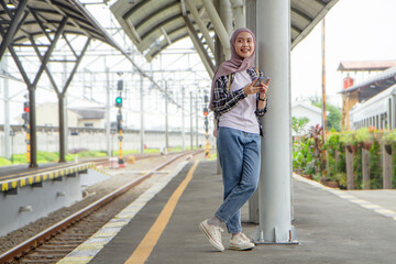 full lenght shoot of asian muslim woman leaning on the pole while holding her mobile phone at train...
