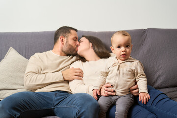 A man and woman are kissing a baby on a couch