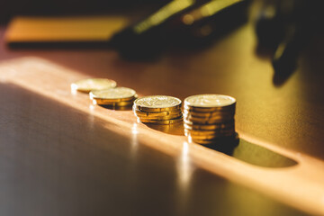 concetti relativi alla contabilità, finanza, economia e matematica. pile di monete di altezza variabile, viste leggermente da sopra e di lato, su un tavolo, illuminate da un raggio di sole