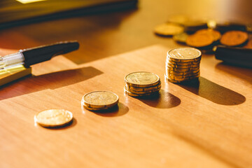 visuale macro di varie file di monete europee su una scrivania di legno, illuminate di lato dalla...