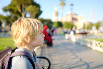 Cute blonde preteen tourist boy sitting on a bench near Sultan Ahmed Mosque district on background...