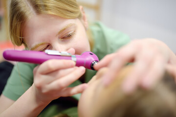 A teenager girl is at an appointment with a caring pediatrician. The doctor ENT is examines nose of a child patient using flashligh.