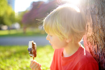 Happy little boy enthusiastically eating tasty ice cream outdoors in summer.