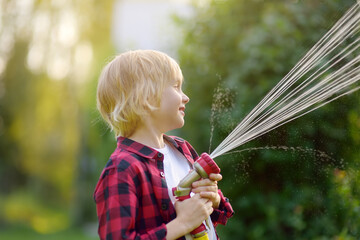 Cute boy watering plants and playing with garden hose with sprinkler in sunny backyard. Preschooler child having fun with spray of water. Summer outdoors activity for kids. Happy childhood. Gardening