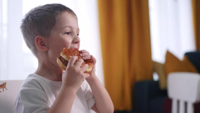 kid preschool boy eats hamburger lifestyle a breakfast at recess. happy family fast food kid dream concept. child son eating hamburger fast food sitting at a table by the window