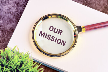 Our Mission symbol. Concept word Our Mission through a magnifying glass on a blank sheet of notepad