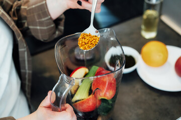 Close up woman adding bee pollen during making smoothie on the kitchen. Superfood supplement....