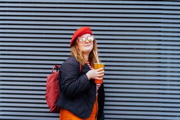 Smiling plus size woman in heart shaped sunglasses and bright clothes drinking sugar flavored...