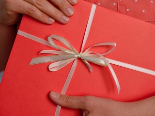 Woman holding a gift in a red wrapping paper with a white bow. Close-up