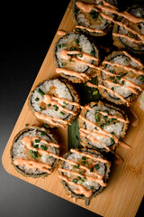 Tempting breaded sushi ensemble on wooden board with sauce and green onions.