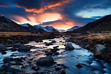 Obraz premium Dramatic sunset over a snowy mountain landscape with a flowing stream