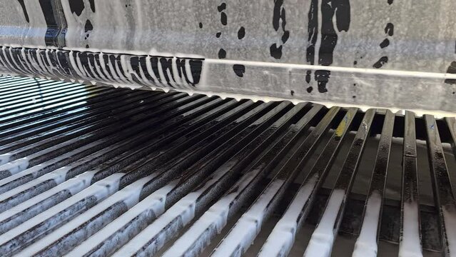 soap foam flows down the surface of a black passenger car during a self-service car wash.