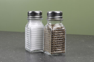 Simple glass restaurant or diner salt and pepper shakers against a green wall