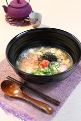 A bowl of Udon noodles with egg, seaweed, and other toppings, served with a teapot and cup