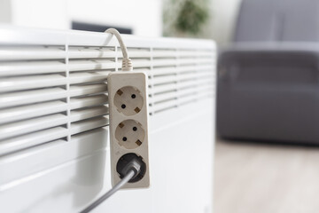 Electric heater plug inserted into extension cord. White radiator for home and office. House heating and comfort