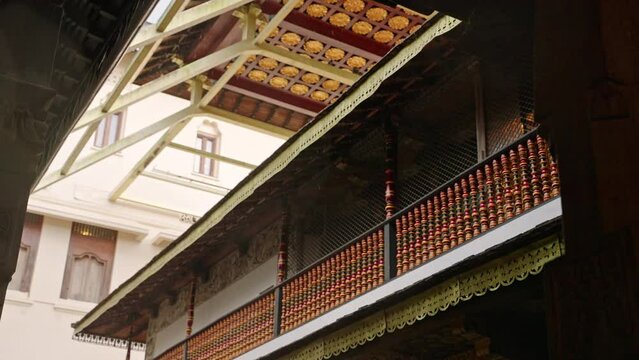 Raindrops fall at Sri Dalada Maligawa Temple as devotees walk barefoot, umbrellas in hand. Serene worship scene, intricate architecture inside sacred hall. Kandy landmark rainy day video. Slow motion.