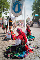 Naklejka premium People in traditional Polish folk costumes at Łowicz Corpus Christi procession. Young women resting sitting on the ground