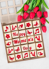 Women's Day dessert. Cute square shortbread cookies with marmalade filling of a thematic shape: Happy Women's Day, flower, heart, butterfly, notes. In a wooden gift box. With red tulips