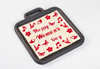 Women's Day dessert. Cute square shortbread cookies with marmalade filling of a thematic shape: Happy Women's Day, flower, heart, butterfly, notes. On a wooden plate