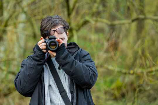 Young photographer teenage girl using DSLR camera outdoors in wood taking photo