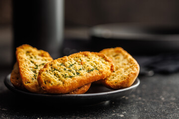 Garlic crisp bread Slices Topped With Herbs onn plate on black table.