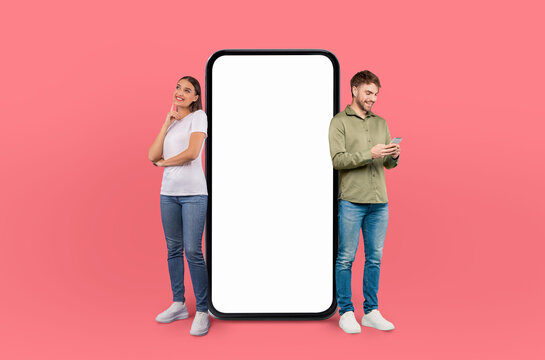 A man and a woman are depicted standing next to a large phone in this scene. They appear to be looking at the phone, possibly engaged in a conversation or using its features