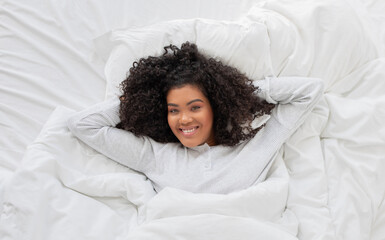 Hispanic woman is laying peacefully in a bed with a white comforter. She appears relaxed and...