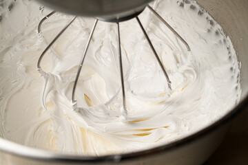 Using a mixer, whipping thick white cream from egg whites and sugar