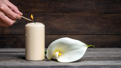 Lighting a candle next to a white calla flower on wood. Day of the dead, all souls day and funeral. Copy space.