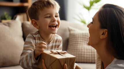 A woman joyfully presents a gift box to a young boy, both smiling in excitement. A heartwarming moment of giving and receiving.