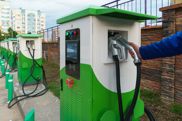 Charging station for electric vehicles. An electric car in the parking lot with a connected connector for charging the battery. Buttons and electronic display of the charging station.
