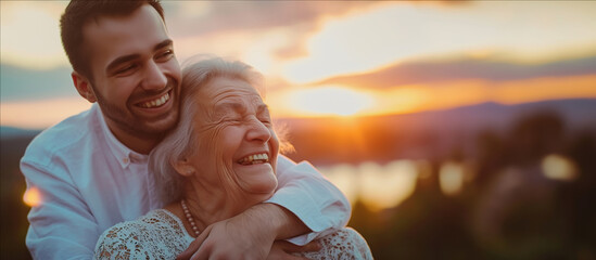 A man tenderly hugs a old mother woman in front of a beautiful sunset.