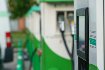 Charging station for electric vehicles. An electric car in the parking lot with a connected connector for charging the battery. Buttons and electronic display of the charging station.