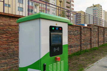 Charging station for electric vehicles. An electric car in the parking lot with a connected connector for charging the battery. Buttons and electronic display of the charging station.