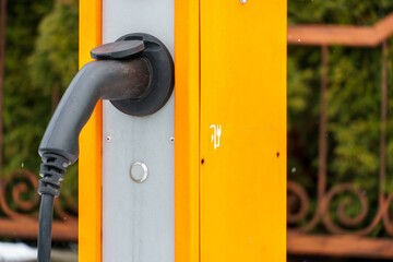 Charging station for electric vehicles. An electric car in the parking lot with a connected connector for charging the battery. Buttons and electronic display of the charging station.