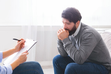 A distressed man is seen with his hand on his mouth as if in deep thought or concern, talking to a...