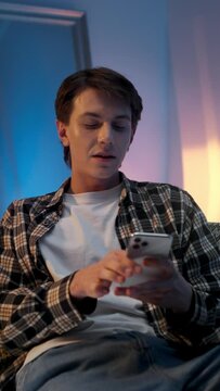 Handsome trendy young model sitting in a armchair and browsing on her mobile phone at the studio