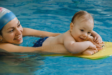 Early age swimming in pool. Baby kid trained to swim in water. Happy child with coach woman in indoor swimming pool playing and having fun. Healthy and sport family with infant, active family
