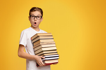 Remote education concept. Shocked schoolboy in glasses holding stack of books, orange panorama...