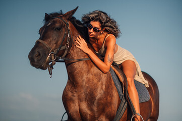 Woman riding a horse on a beach during a sunset and leaning up front to pet it